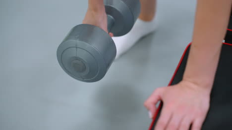 close-up of woman performing dumbbell row, engaging arm muscles while balancing on one leg, focus on grip strength, controlled movement, and stability during workout in gym environment