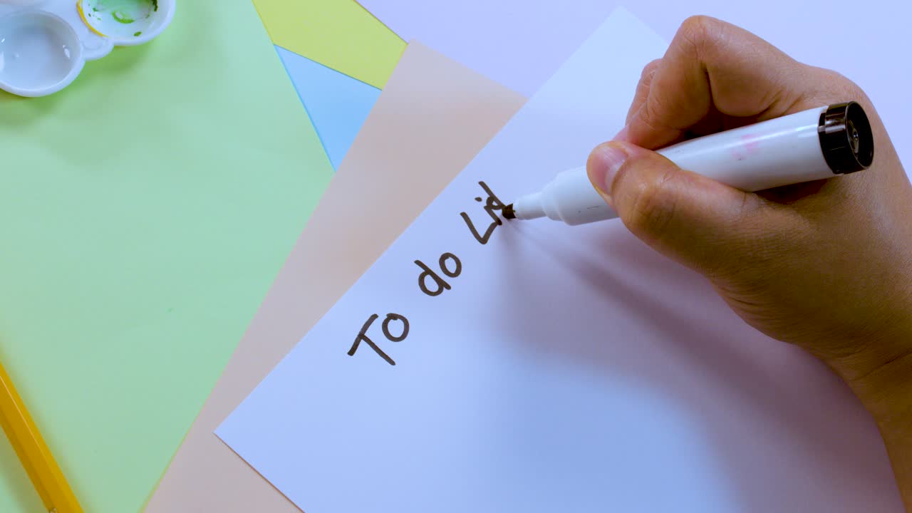 Person writes 'To do List' on white paper with marker, overhead view, bright lighting