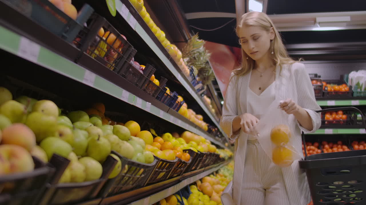 A beautiful blonde in the supermarket chooses oranges and puts them in a bag to weigh on the scales.
