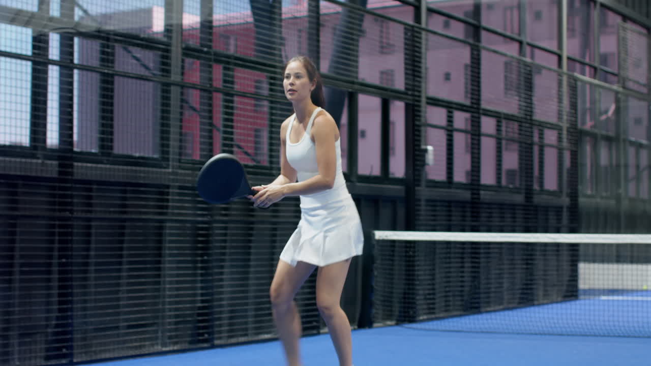 Woman playing padel tennis, swiftly moving on indoor court, focused on game