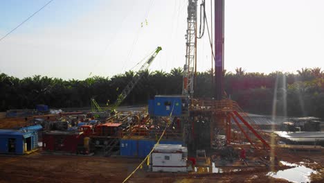 Cinematic-4K-Drone-Footage-of-Onshore-Drilling-Rig-equipment-structure-for-oil-exploration-and-exploitation-in-the-middle-of-jungle-surrounded-by-palm-oil-trees-during-sunset-and-high-oil-price