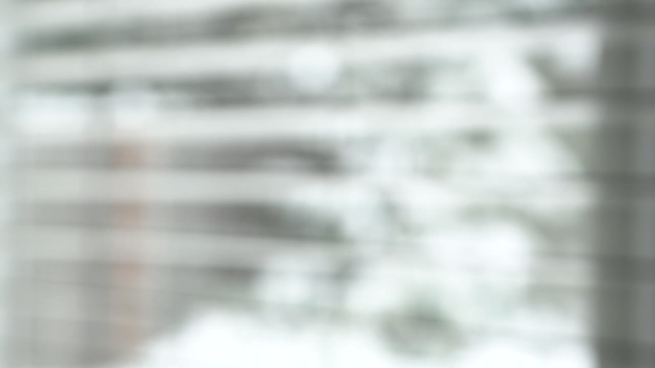 Rack focus of snow falling in backyard, looking out through window blinds