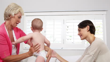 madre y abuela jugando con el bebé en una cama