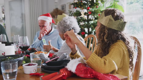 familia de varias generaciones jugando con novedades de galletas de navidad mientras se sientan a comer en la mesa