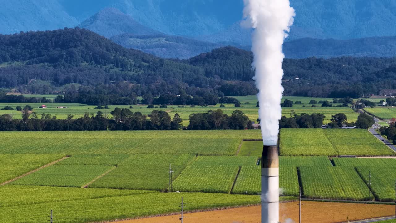Aerial footage of sugarcane fields with a factory emitting smoke, captured in bright daylight over Tweed River, Gold Coast
