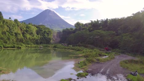 aerial view of natural lake and driving old truck on pebbly road in bego pendem,indonesia - beautiful forest landscape and merapi volcano in background