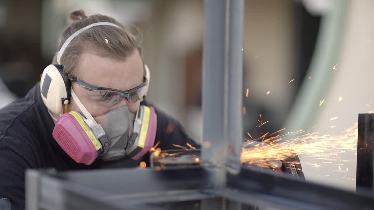 мужчина-металлист в респираторе режет металлические конструкции угловой шлифовальной машиной