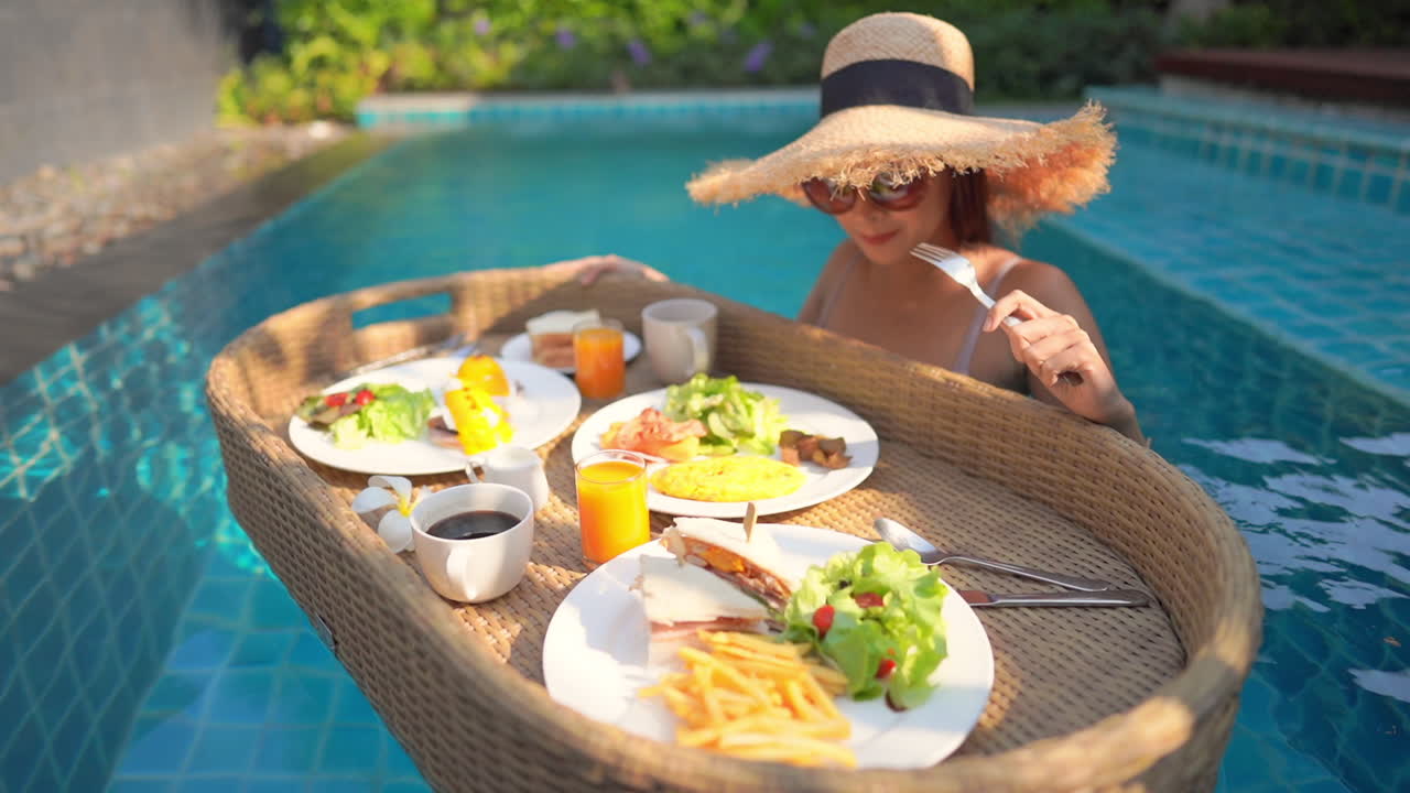 A young woman tourist has her own personal breakfast on a floating table in a private swimming pool. Tropical beach lifestyle