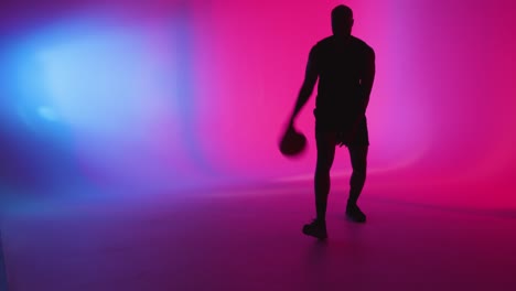 silueta de estudio de un jugador de baloncesto masculino driblando y rebotando la pelota contra un fondo iluminado de rosa y azul 2