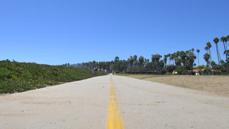 Standing-on-the-beach-bike-path-with-two-bikers-riding-together-in-the-distance-along-the-coast-on-a-sunny-clear-day-in-Santa-Barbara,-California