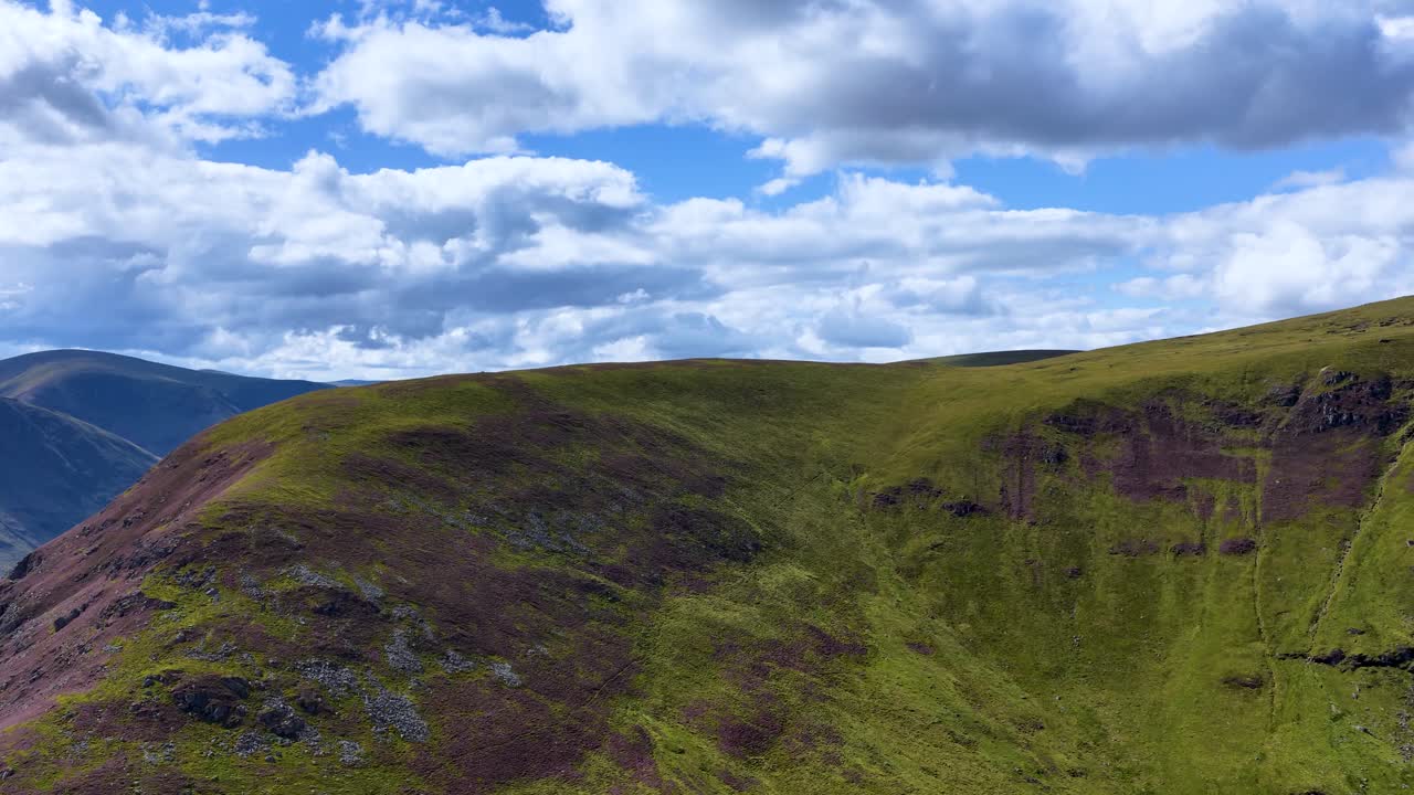 Drone camera smoothly pans across green mountain ridge under dramatic clouds, daylight, Highlands, Scotland