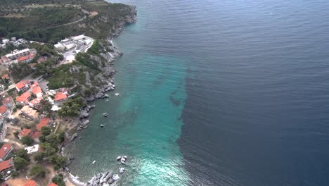 Aerial-view-of-turquoise-beach-with-rocks-under-a-tourist-village-in-the-area-of-Agia-Paraskevi-Halkidiki,-Greece,-circular-movement-by-drone