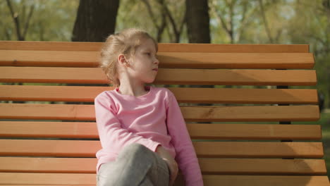 upset little girl sits and fans away bug on bench in park