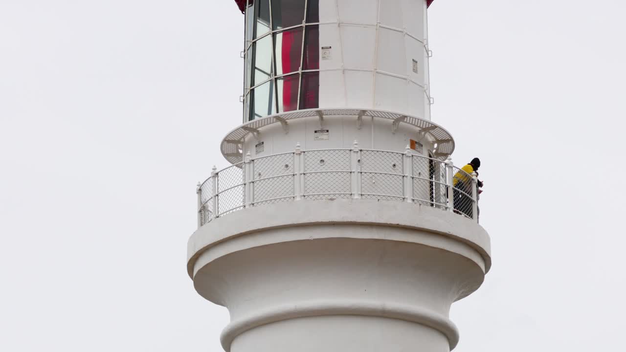 A person observes from a lighthouse balcony under overcast skies, capturing the serene coastal atmosphere