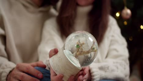 close-up shooting, the girl turns over the glass new year's sphere and the sparkles in it begin to spin and fly beautifully. a guy and a girl play with a new year's glass sphere during their evening date during the new year