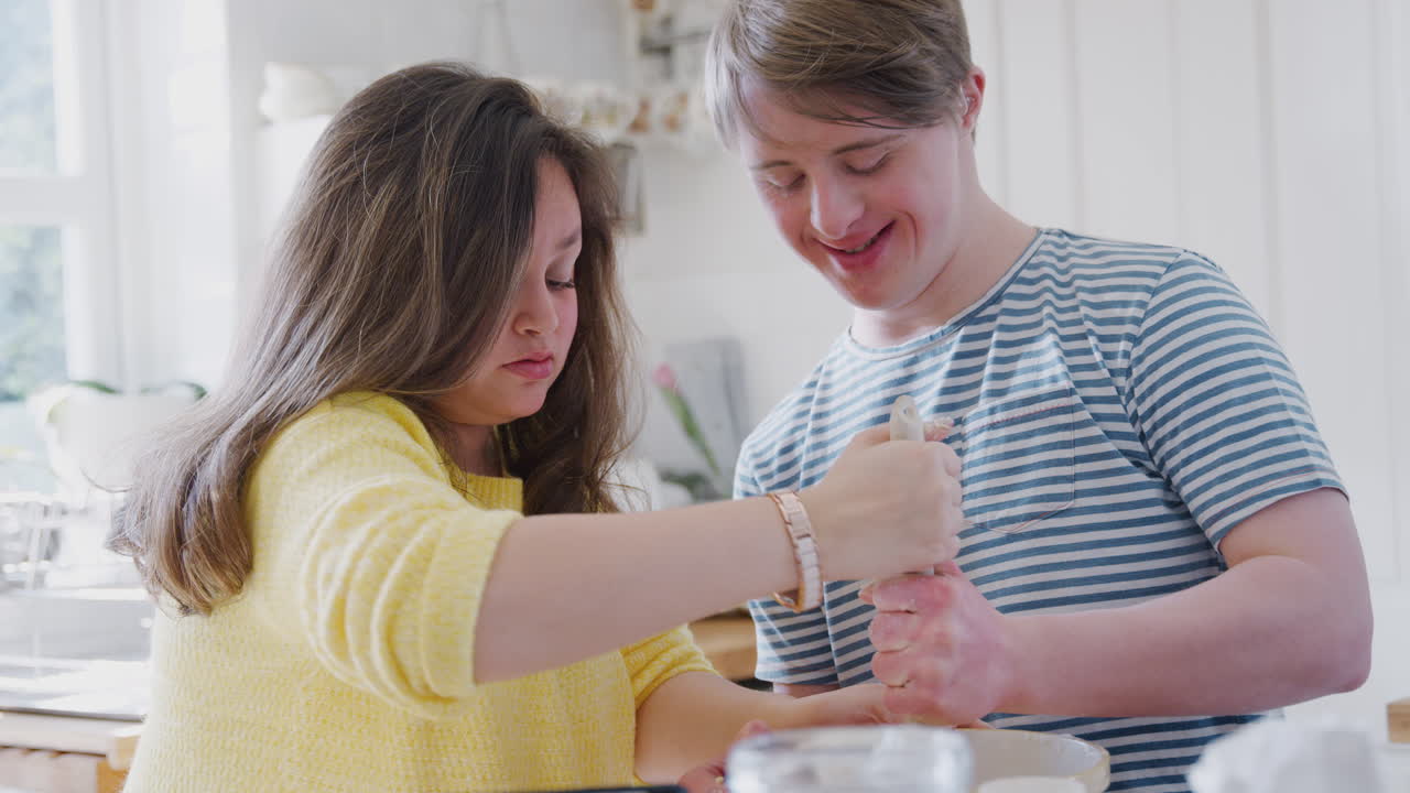 una pareja joven con síndrome de down mezcla ingredientes para una receta de pastel que están horneando en la cocina en casa.