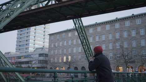 man relaxes on river bridge while wuppertal suspended train passes by