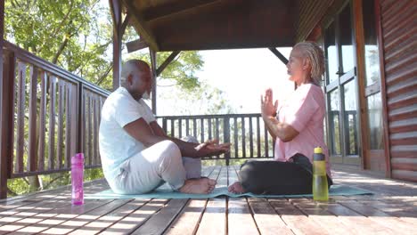 focused senior african american couple holding hands practicing yoga on sunny terrace, slow motion