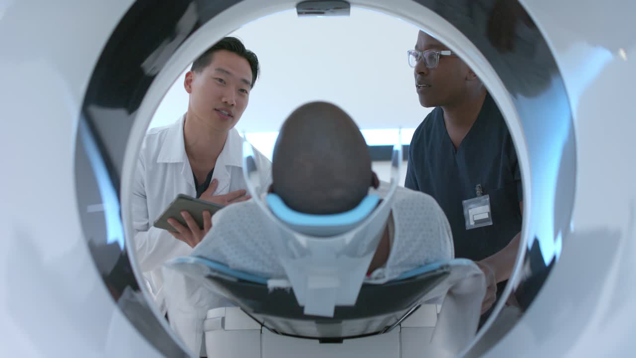 Team eterogeneo che prepara un paziente maschio afroamericano per una scansione alla testa nel tunnel della risonanza magnetica usando un tablet