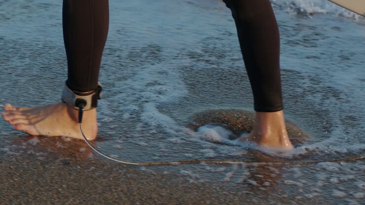 Un surfista che cammina verso la spiaggia al tramonto per prepararsi all'allenamento di surf e cercare le onde a Barcellona, Spagna, acqua, esercizio fisico in mare con la tavola, vacanza o viaggio di un uomo atletico.