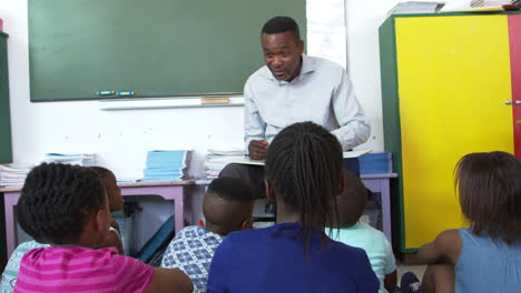 elementary school kids sitting on floor listening to teacher