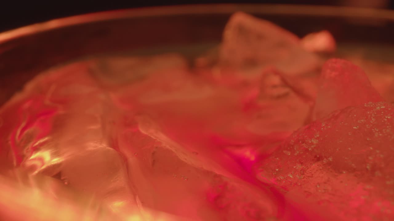 Close up of Whiskey glass filled with ice and liquid slides right then left across camera