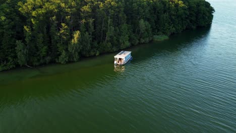 Casa-Flotante-Flotando-En-Un-Lago-Junto-A-Una-Enorme-Isla-Cubierta-De-árboles-En-Brandeburgo,-Alemania