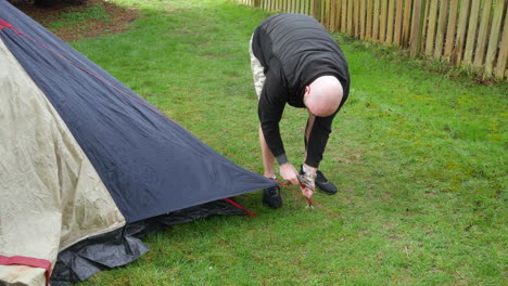 a man removing pegs from guy ropes on a tent at a campsite