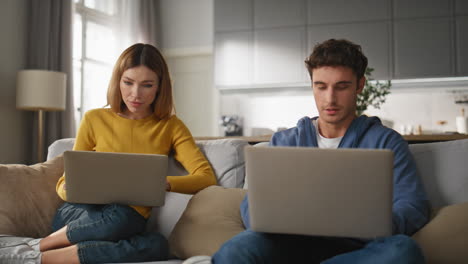 Involved pair working computers at couch closeup. Couple solving tasks together