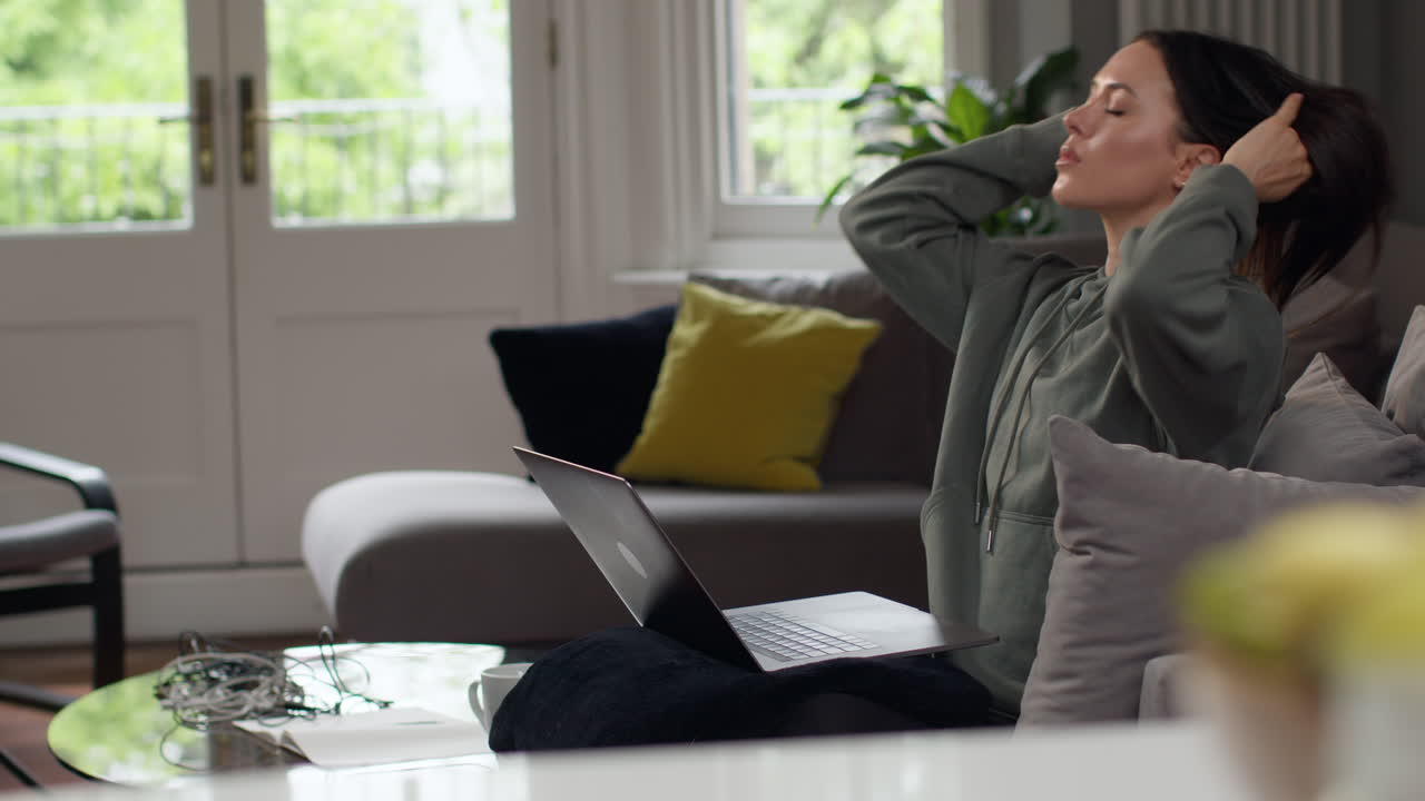 소파에 앉아 집에서 노트북을 사용하고 생활비 위기에 대해 걱정하는 불안한 여성