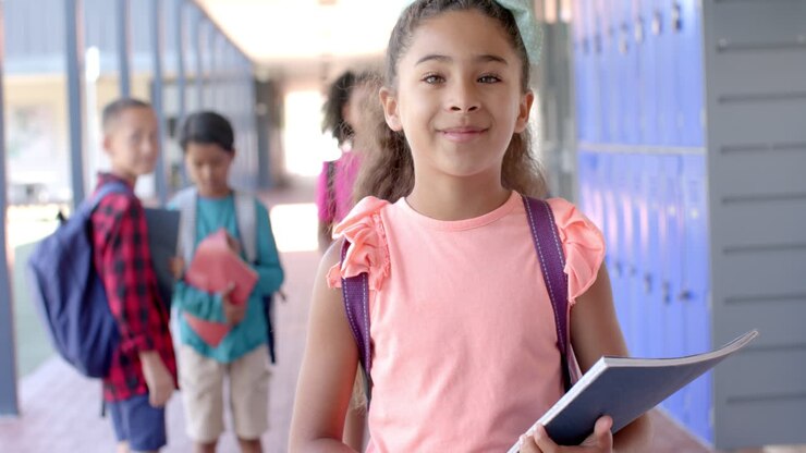 En un pasillo escolar, una joven afroamericana sostiene un libro.