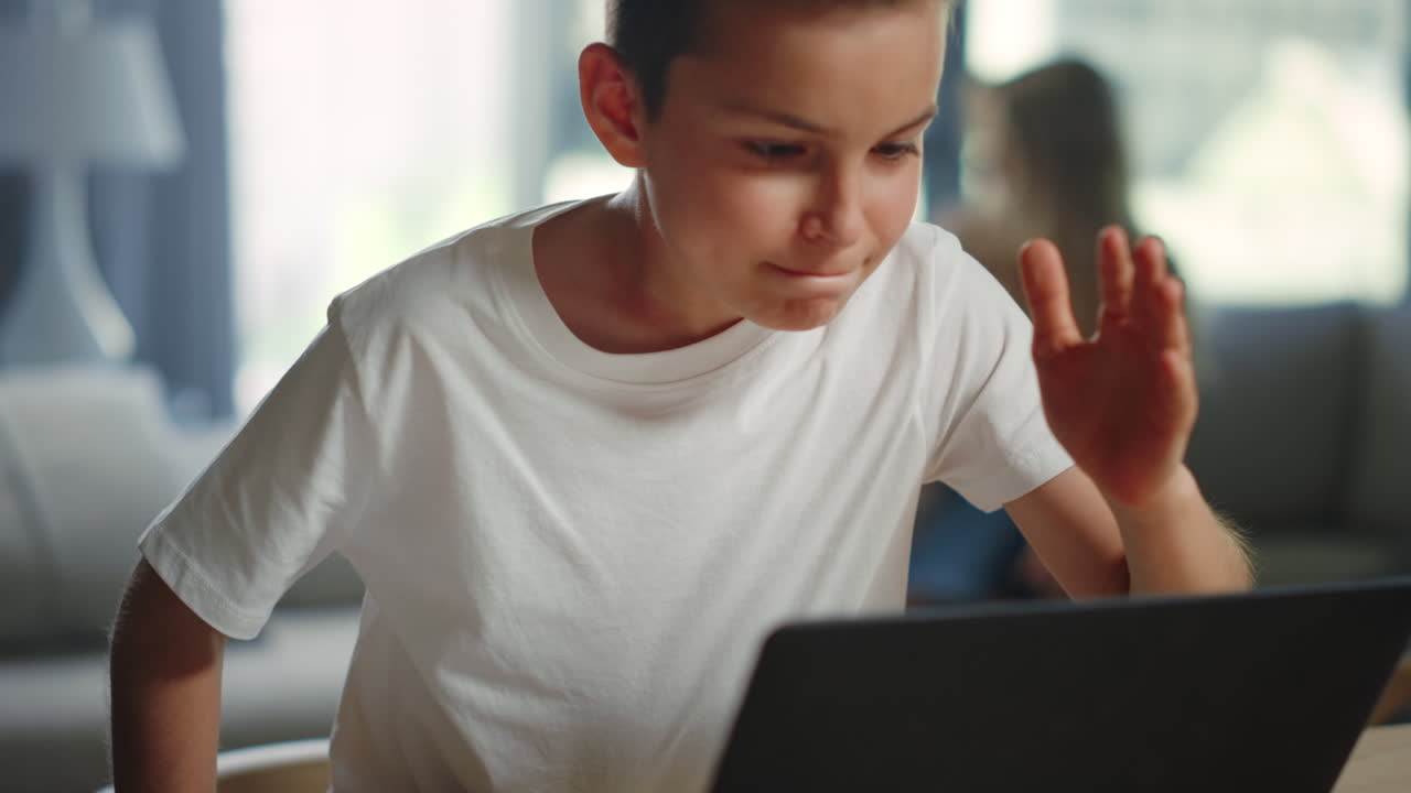 Bambino che alza la mano durante una lezione video al chiuso. Ragazzo attivo che impara a distanza.
