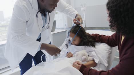 Diverse-doctor-putting-oxygen-mask-on-sick-girl-patient-with-mother-in-hospital-in-slow-motion