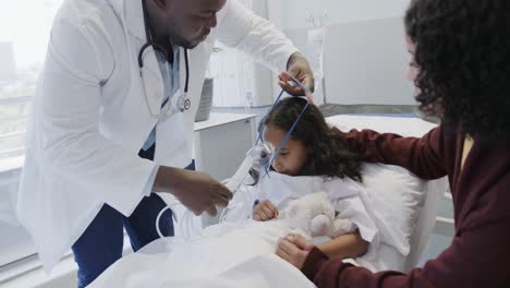 diverse doctor putting oxygen mask on sick girl patient with mother in hospital in slow motion