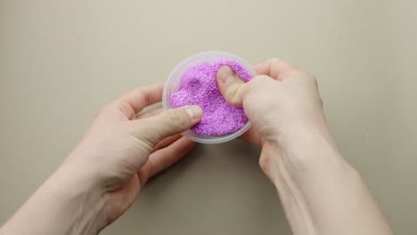 pressing purple foam slime into clear plastic container, pov