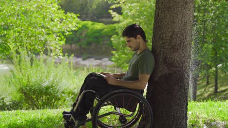 un adolescente sentado en una silla de ruedas está leyendo un libro.