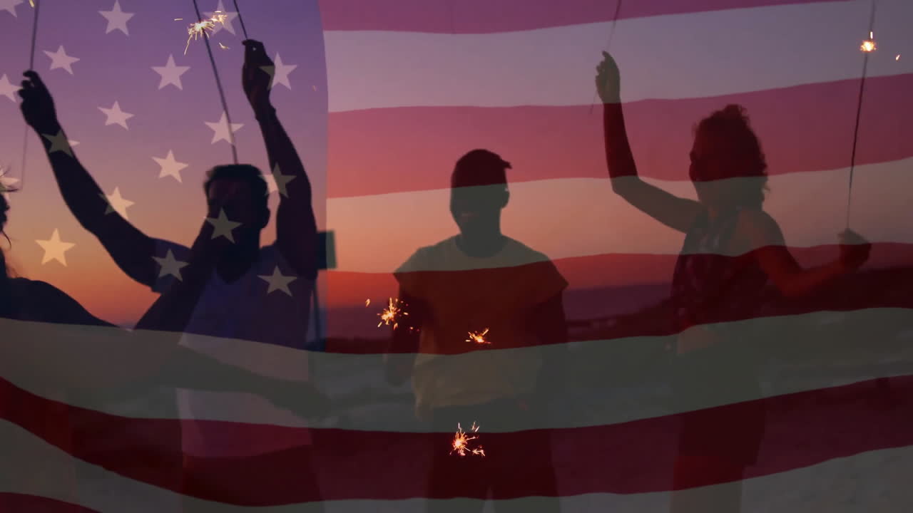 Animation of flag of america over happy diverse friends dancing with sparklers on sunset beach