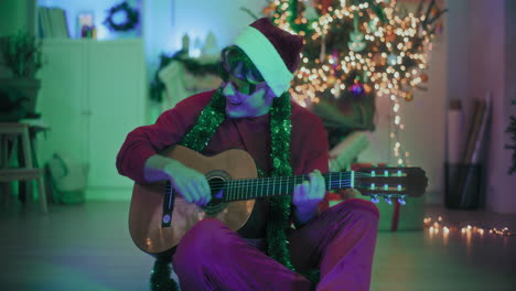 hombre tocando la guitarra mientras está sentado en el suelo en una casa iluminada durante la navidad