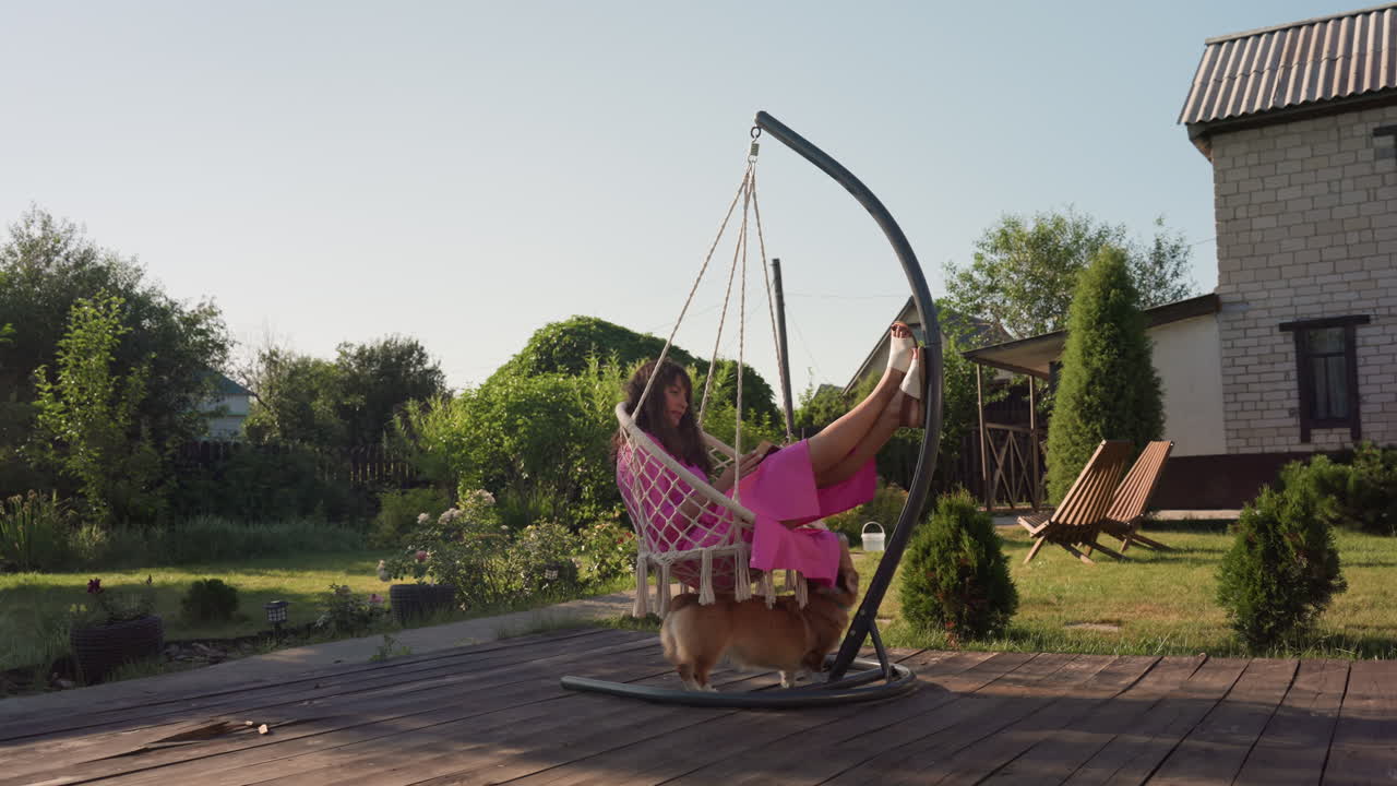 Lady In Rosy Gown Outdoors, Female Resting On Porch Swing Outdoors, Woman In Pink Dress Enjoys Sunny Backyard Rest, Woman Dressed In Pink Reclines On Swing In Warm Sunny Backyard Setting
