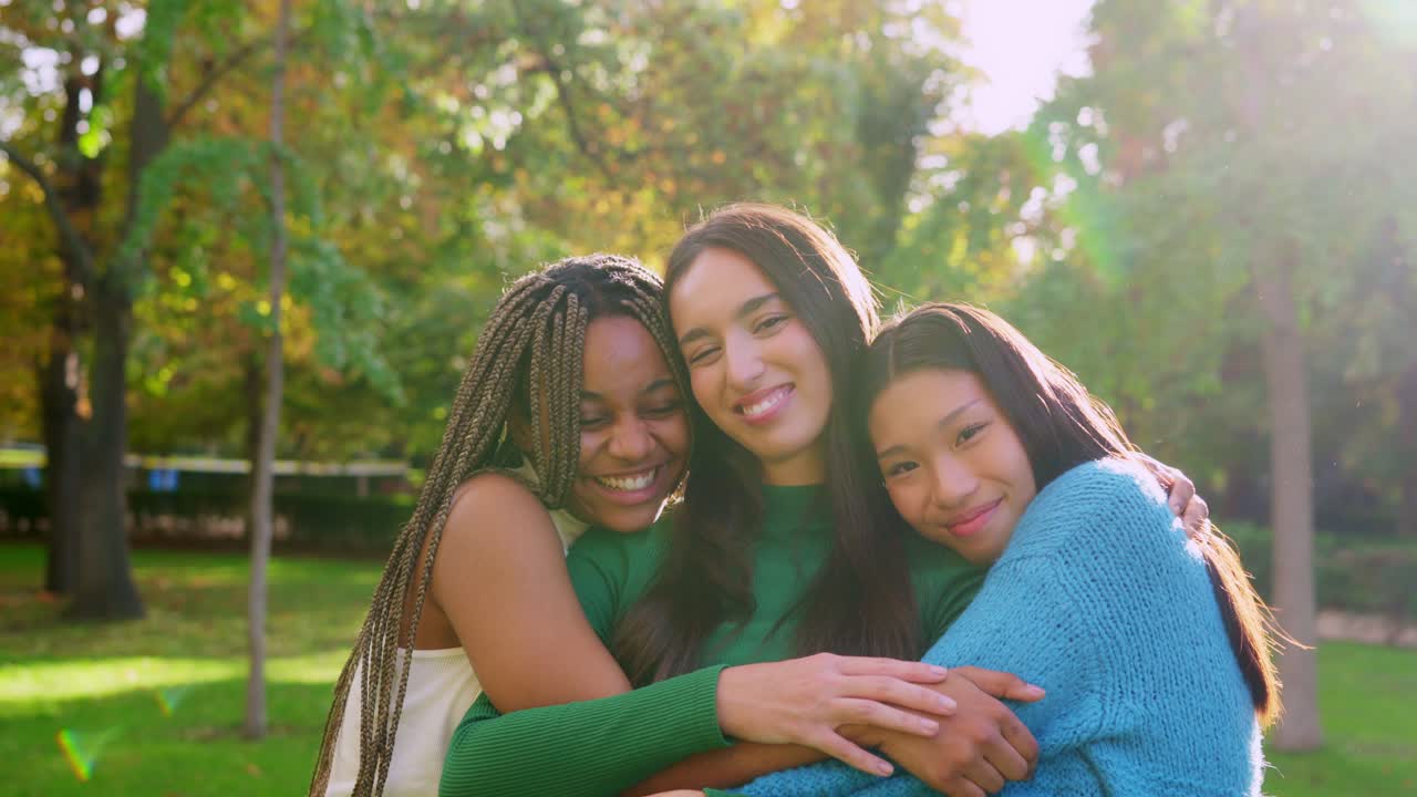 Três jovens mulheres diversas se abraçando felizes em um parque