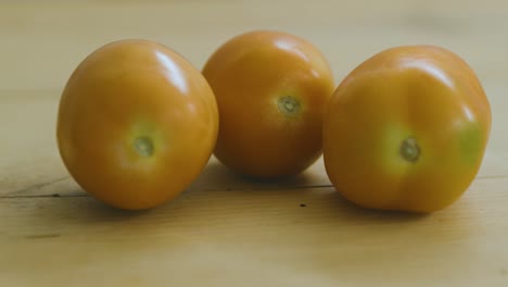 dos tomates sobre una mesa de madera, otro llega rodando.