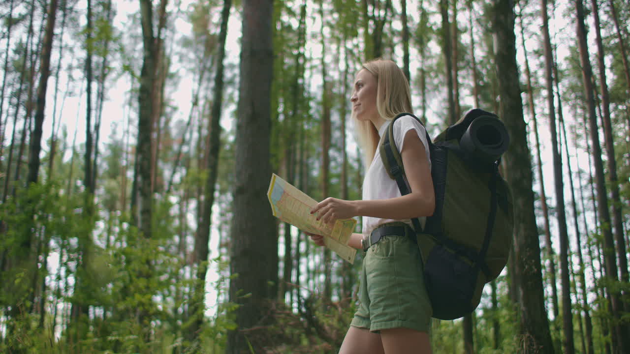 joven mujer caucásica buscando la dirección en un mapa mientras caminaba en el bosque. chica feliz mientras caminaba en la naturaleza y orientándose con la ayuda de un mapa