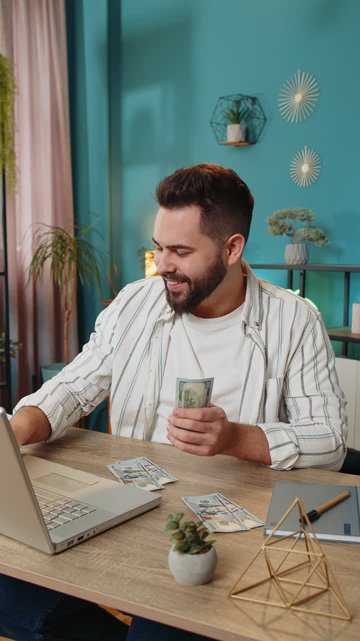 Happy rich business man counting money cash dividends salary and using laptop in home office