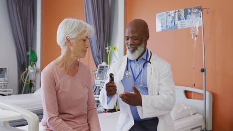 African-american-male-doctor-showing-senior-caucasian-female-patient-otoscope-at-hospital