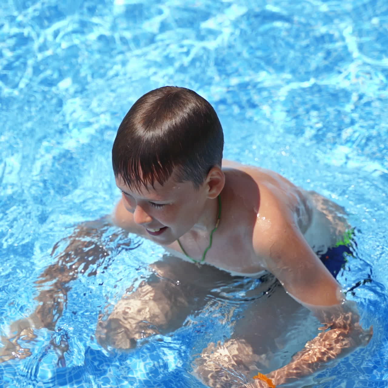 Boy swimming in the pool. Teenager swims underwater in the swimming pool. Child having fun in the water park in a sunny day.