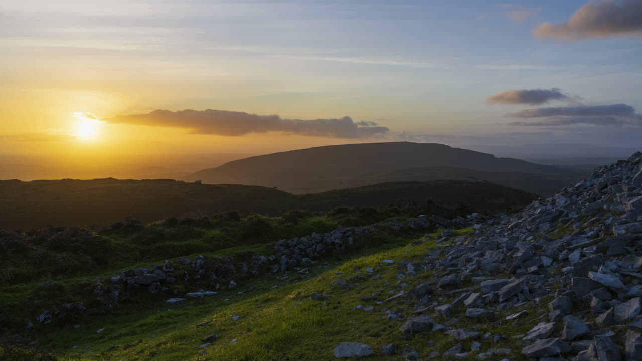 lapso de tiempo del paisaje de la naturaleza rural con colinas en la distancia durante la noche con el sol detrás de las nubes visto desde la tumba del pasaje prehistórico de carrowkeel en el condado de sligo en irlanda