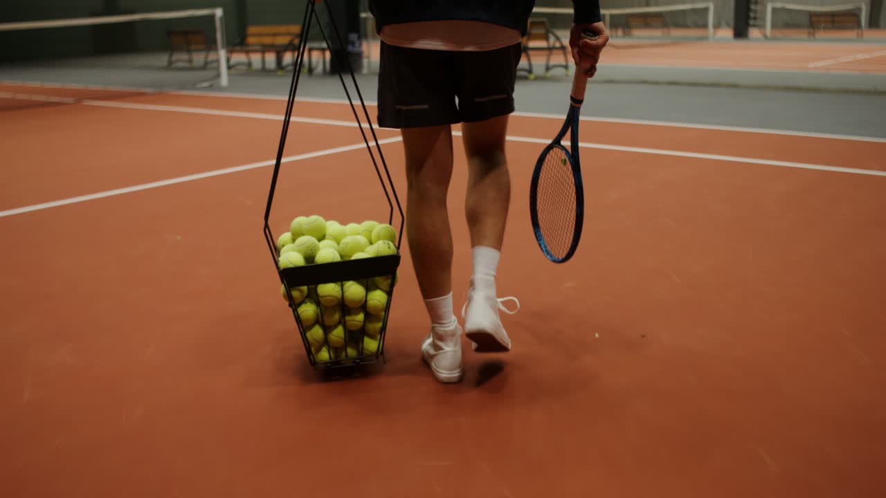 Tennis player carrying a basket of tennis balls