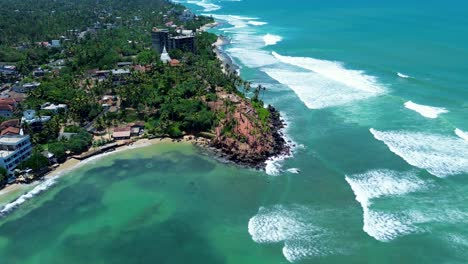 aerial drone of coconut tree hill bay palm plantation on headland coastline with local town village indian ocean waves mirissa point sri lanka asia