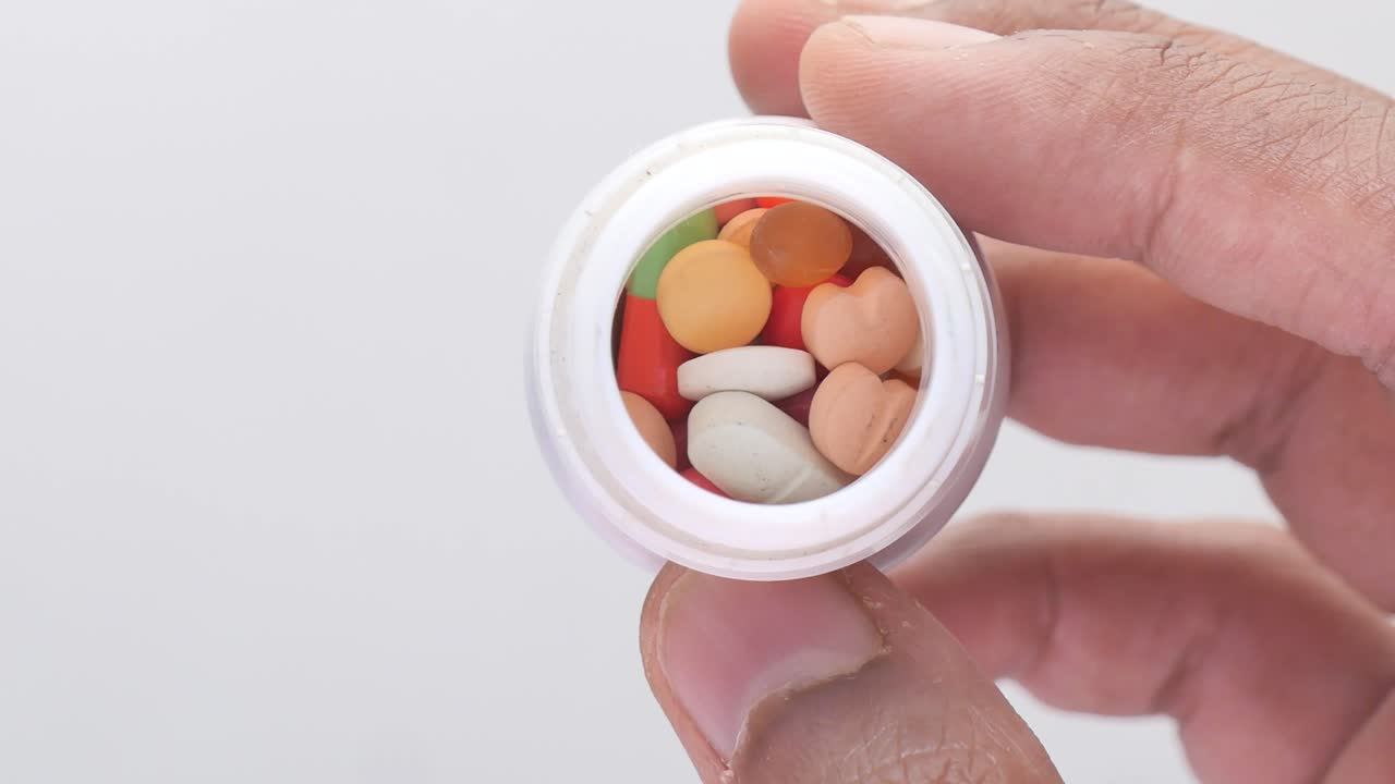 primer plano de una mano sosteniendo un frasco de pastillas y cápsulas variadas