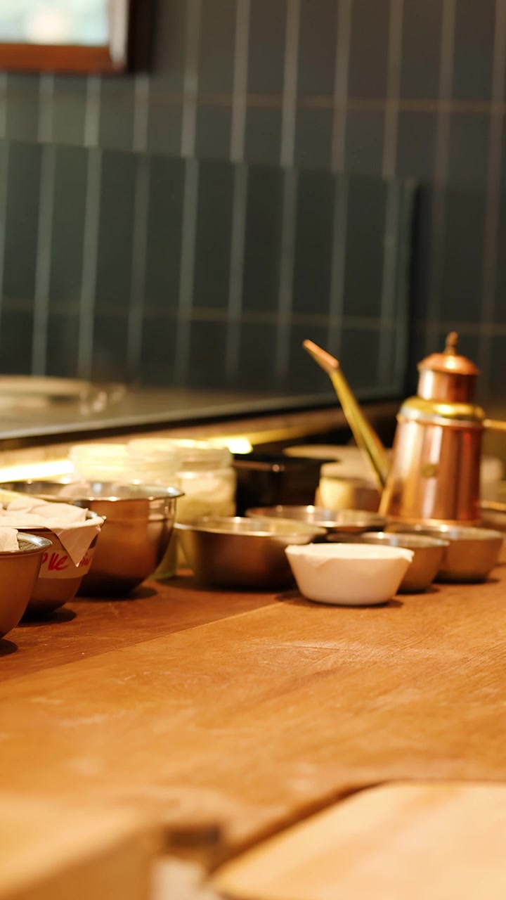 Slow camera pan across a wooden kitchen counter with stainless steel bowls and copper oiler.
